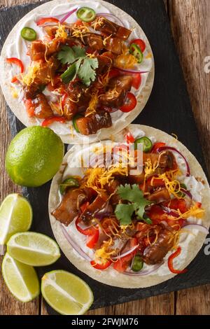 Tacos avec poitrine de porc frite, légumes, sauce chaude, fromage et citron vert sur un tableau d'ardoise sur la table. Vue verticale du dessus Banque D'Images