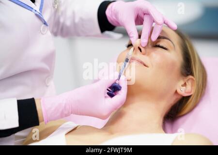 Médecin effectuant la rhinoplastie par injection d'acide hyaluronique dans le nez de son patient. Banque D'Images