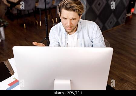 Confus jeune travailleur indépendant caucasien de sexe masculin regarder l'écran d'ordinateur choqué par la panne de gadget ou des problèmes opérationnels. Frustré par l'homme Banque D'Images