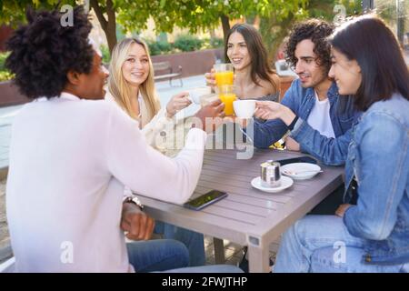 Groupe multiethnique d'amis qui toaster avec leurs boissons tout en prenant un verre ensemble. Banque D'Images