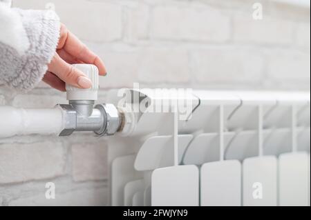 Gros plan d'une main femelle régulant la température d'un radiateur de chauffage Banque D'Images