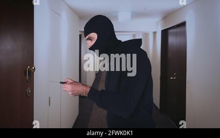 Voleur avec balaclava tente d'ouvrir la porte de l'appartement avec une clé Banque D'Images