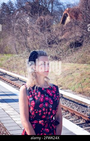 femme blonde en robe rouge attendant à la gare Banque D'Images