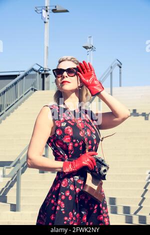 élégante femme blonde dans une robe rouge avec un appareil photo vintage debout à l'extérieur Banque D'Images
