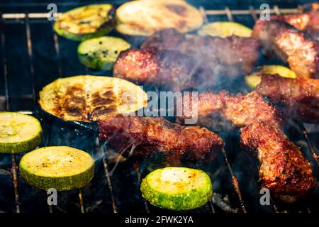 Griller des rouleaux de viande appelés mici ou mititei avec des légumes sur barbecue à l'omble. Barbecue au charbon de bois avec feu de cheminée Banque D'Images