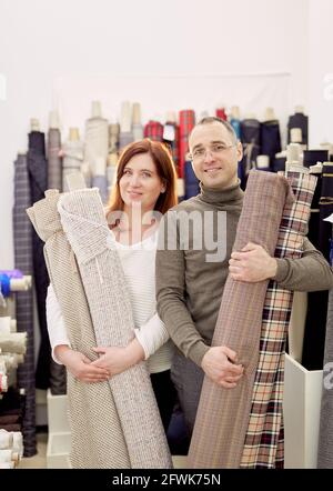 Couple de deux tailleurs professionnels ou des concepteurs debout et tenant des rouleaux de lin textile et regardant à la caméra. Équipe d'affaires familiales travaillant ensemble. Couture, travaux d'aiguille ou concept de couture Banque D'Images