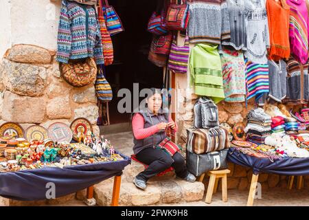 Femme quechua locale assise à l'entrée d'une boutique de souvenirs touristiques, Chinchero, un village rustique andin, Vallée Sacrée, Urubamba, région de Cusco Pérou Banque D'Images