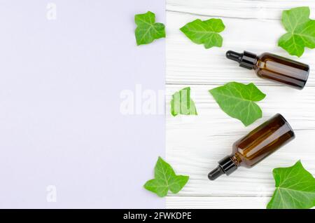 Concept pour la production de produits à partir d'ingrédients naturels et de médicaments de remplacement. Deux bouteilles brunes avec des huiles et des feuilles de lierre sur un bois clair Banque D'Images