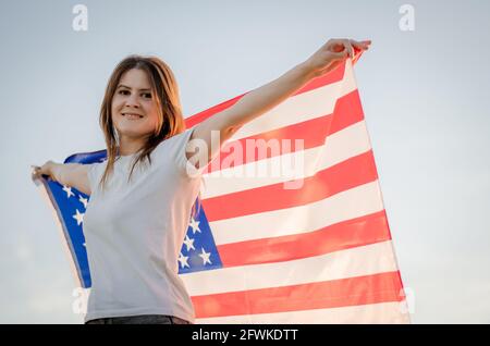 Belle jeune femme avec le drapeau national de l'Amérique dans ses mains contre le fond du ciel. 4 juillet, jour de l'indépendance. Américain fredo Banque D'Images