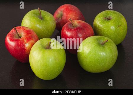 Plusieurs pommes, certaines sont vertes et d'autres sont rouges. Ils sont sur un banc en granit noir dans une cuisine. Banque D'Images