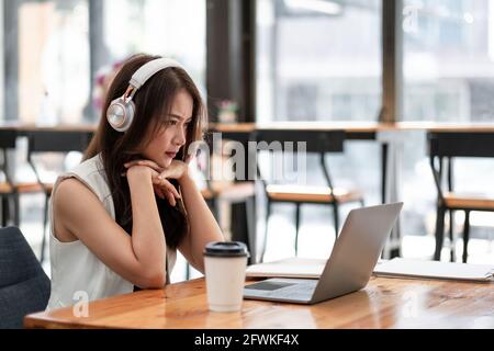 Jeunes femmes asiatiques concentrées portant un casque regarder l'ordinateur portable pour l'étude en ligne, attrayante femme étudiant en langue d'apprentissage, regarder en ligne Banque D'Images