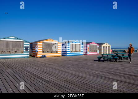 Idée de Staycation. Des stands colorés de style cabane de plage à rayures dans une rangée sur la jetée de Hastings, East Sussex, Angleterre, Royaume-Uni. Banque D'Images