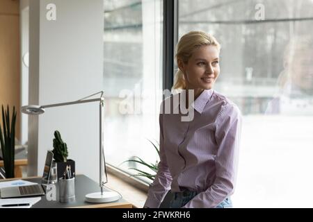 Rêveuse femme d'affaires souriante qui cherche à côté au bureau Banque D'Images