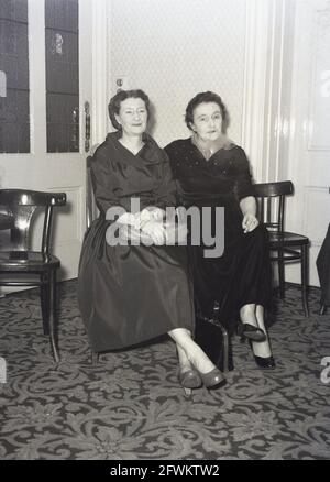 1957, historique, lors d'une fête d'entreprise à l'intérieur d'une salle de réception à l'hôtel Victoria, Leeds, deux femmes matures dans des robes de soirée élégantes, assis ensemble pour leur photo, Angleterre, Royaume-Uni. Banque D'Images