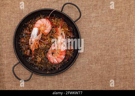 Recette pour le riz, le poisson, les fruits de mer et l'encre de calmar cuits dans une petite paella sur une surface en toile de raclage. Il y a deux grandes crevettes et il est prêt à manger. Banque D'Images