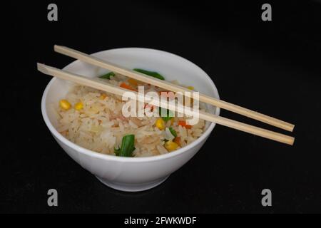 Trois délicieux riz chinois aux crevettes, aux haricots verts, au maïs et aux carottes, servis dans un bol blanc sur lequel il y a deux baguettes. Banque D'Images