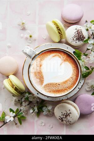 Macarons avec une tasse de café et une branche de fleurs blanches sur fond de carreaux roses. Dessert français et fleurs Banque D'Images