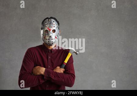 Studio portrait d'un homme inconnu sur fond gris qui est habillé d'un masque maniaque effrayant. Banque D'Images