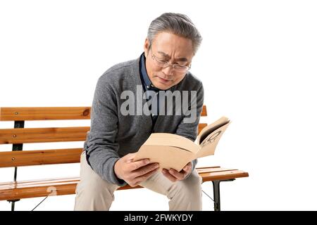 Assis sur un banc dans le vieil homme lisant un livre Banque D'Images