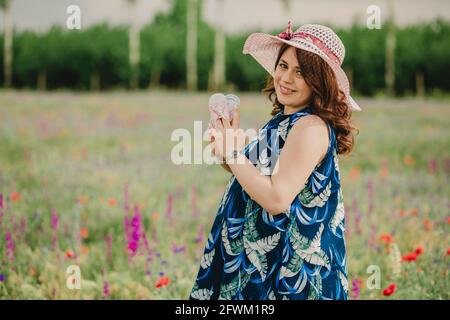 Gros plan de la jeune femme souriante et de la future maman. Tenant ses chaussures de bébé et regardant l'appareil photo dans le champ plein de fleurs Banque D'Images