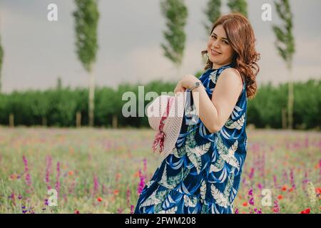 Portrait d'une femme enceinte tenant son chapeau plein sur le terrain de fleurs en été et profiter du temps chaud Banque D'Images