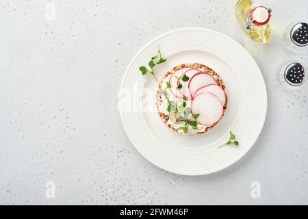 Gâteau au sarrasin croustillant sans gluten avec fromage à la crème, radis rouge et micro-vert pour un petit déjeuner sain sur fond de pierre grise. Vue de dessus. Banque D'Images