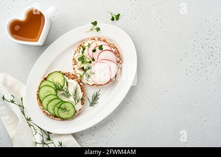 Deux gâteaux croustillants de sarrasin sans gluten avec fromage à la crème, radis rouge, concombre et microgreen pour un petit déjeuner sain sur fond de pierre grise. VI Banque D'Images