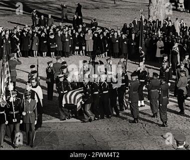 Les pallbearers de la garde d'honneur portent le cercueil à pavillon du président John F. Kennedy sur la tombe du cimetière national d'Arlington, pendant les services de tombes des funérailles d'État du président Kennedy. Marche en procession : archevêque de Washington, Patrick A. O’Boyle; président des chefs d’état-major interarmées, général Maxwell D. Taylor; chef d’état-major de l’Armée de l’air des États-Unis, général Curtis E. LeMay. Les officiels et les dignitaires observent, notamment : le sénateur Kenneth B. Keating (New York); le sénateur Daniel Inouye (Hawaii). Banque D'Images