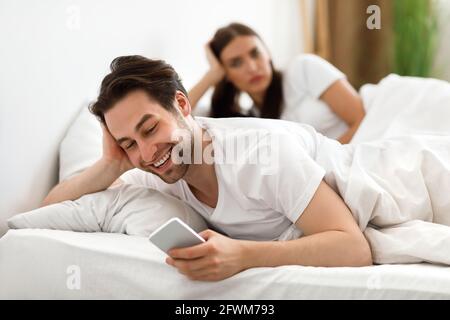 Tricherie mari textant sur téléphone ignorant femme couché dans le lit Banque D'Images