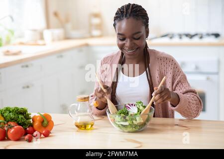 Concept de régime sain. Jeune femme afro-américaine joyeuse cuisant de la salade de légumes frais Banque D'Images