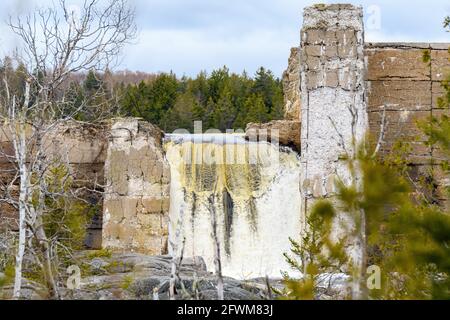 L'eau coule sur un vieux barrage brisé. Le barrage est en train de s'écrouler et est vu à travers les arbres. Ciel couvert. Banque D'Images