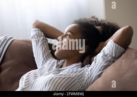 Jeune femme afro-américaine rêveuse se détendant sur un confortable canapé. Banque D'Images