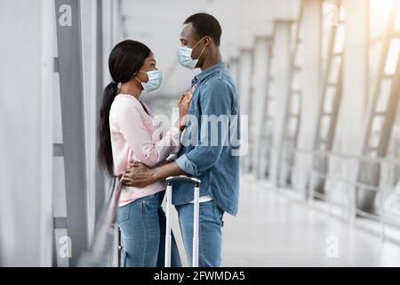 Bonne Réunion. Heureux couple noir dans masques médicaux de protection embrassant à l'aéroport Banque D'Images