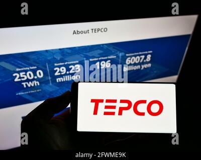 Personne tenant un téléphone portable avec le logo de Tokyo Electric Power Company Holdings Inc. (TEPCO) à l'écran en face de la page Web. Mise au point sur l'affichage du téléphone. Banque D'Images
