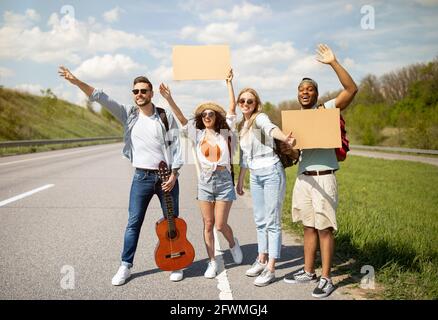 Groupe d'amis multiraciaux avec guitare et panneau vide hitchranking sur la route, la descente en voiture, voyage en autostop Banque D'Images