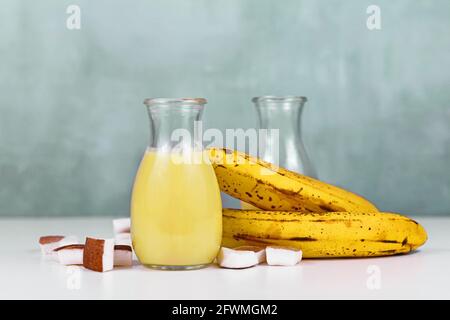 Boisson fouettée à la banane et à la noix de coco dans un pot sur une table blanche à côté des ingrédients Banque D'Images