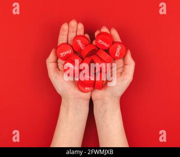 Kharkov, Ukraine - Mai 16, 2021: Beaucoup de Coca Cola casquettes en main de la femme sur un fond rouge et vue de dessus Banque D'Images