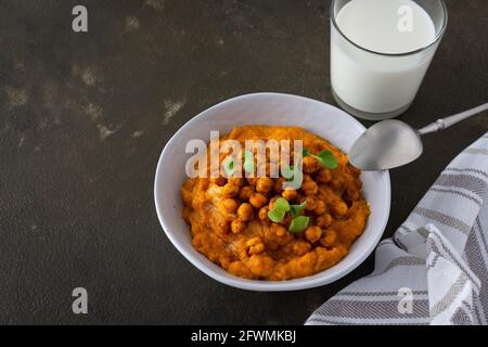 Soupe de potiron épaisse aux pois chiches cuits et aux pousses de radis dans une assiette avec un verre de lait sur la table, délicieux dîner sain Banque D'Images