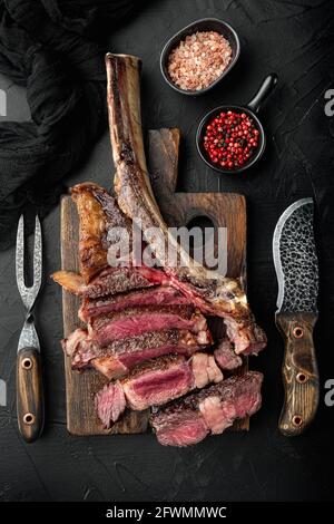 Ensemble de steaks de bœuf tomahawk en tranches grillées, sur une planche de service en bois, sur fond de pierre noire, sur une surface plane avec vue du dessus Banque D'Images