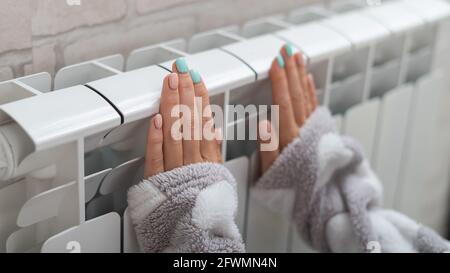 Une femme portant un pyjama chauffe les mains froides sur le radiateur de chauffage Banque D'Images