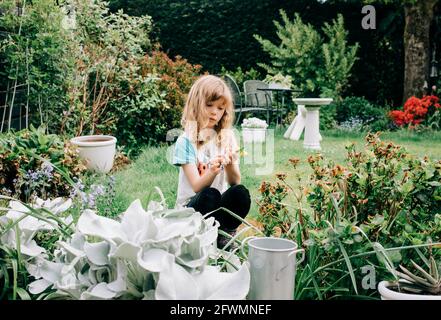 une fille s'est assise dans une belle cour arrière cueillant des fleurs à la recherche réfléchi Banque D'Images