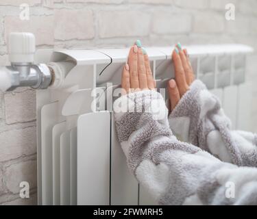 Une femme portant un pyjama chauffe les mains froides sur le radiateur de chauffage Banque D'Images