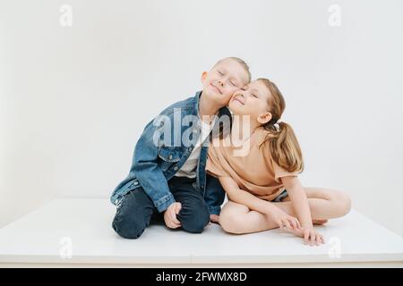 Des frères et sœurs en cuddling assis sur une table, des joues pressantes dans le bonheur, l'amour et l'appartenance Banque D'Images