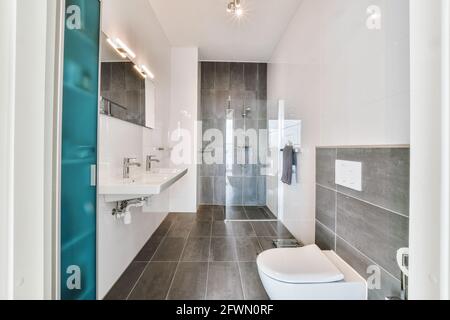 Décoration intérieure contemporaine de la salle de bains avec sol carrelé et murs blancs avec cabine de douche derrière le mur de verre et toilettes et lavabo Banque D'Images