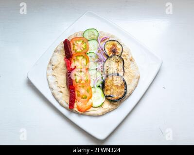 Sandwich libanais servi avec du houmous, des tranches de tomate, de concombre, d'aubergine, de betterave et d'oignon rouge sur une surface blanche Banque D'Images