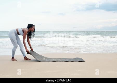 Jeune sportif souriant, il fait rouler le tapis de yoga sur du sable plage pour le yoga ou la méditation le matin Banque D'Images
