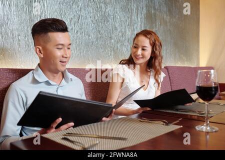 Un jeune couple souriant boit du vin et lit un menu qui décide quoi à commander pour le dîner au restaurant Banque D'Images