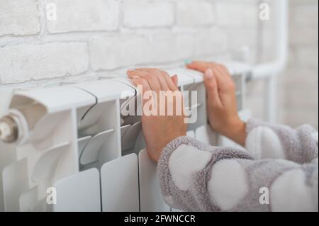 Une femme portant un pyjama chauffe les mains froides sur le radiateur de chauffage Banque D'Images