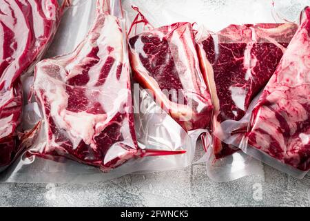 Steak de bœuf scellé sous vide prêt pour la cuisson sous vide, le tomahawk, le t-bone, le steak de club, les yeux de côtes et les coupes de filet, sur fond de pierre grise Banque D'Images