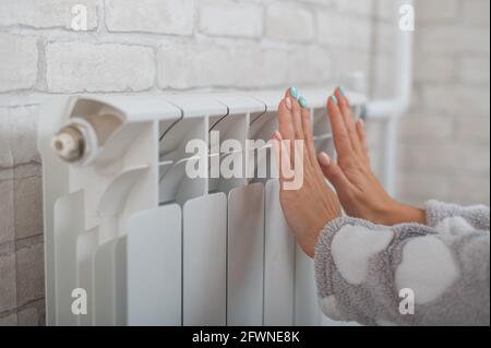 Une femme portant un pyjama chauffe les mains froides sur le radiateur de chauffage Banque D'Images